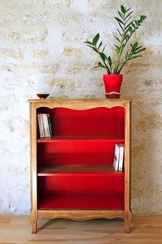 a red book shelf with a potted plant on top