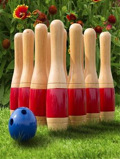 several wooden bowling pins lined up next to a blue ball on the grass with flowers in the background