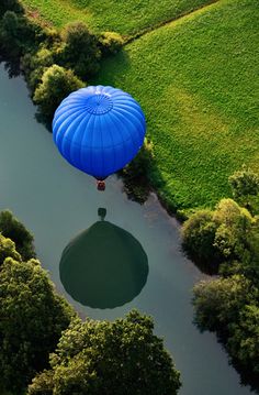 a hot air balloon floating over a river in the middle of a lush green field