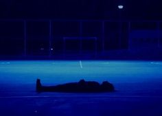 a person laying on the ground in front of a soccer field at night with blue lights