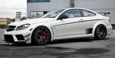 a white sports car parked in front of a building with red rims on it