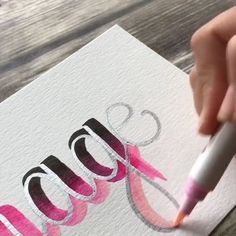 a hand holding a marker writing the word mom on a piece of paper with pink and black ink