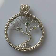 a silver brooch with a tree in the center and green stones on each side