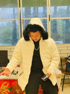 a man in a white jacket and black pants standing next to a table with a cell phone