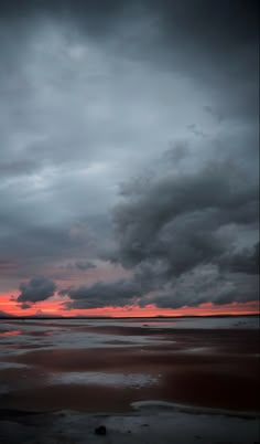 the sky is dark and cloudy as the sun sets on the horizon in the distance