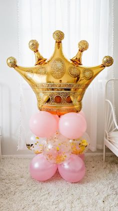 a gold crown sitting on top of balloons in front of a white bed and window