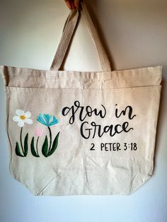 Handpainted and handlettered tote bag. Perfect for a Bible bag, book bag, or for carrying essentials! It has a rectangular shape with a large main pocket and two braided handles on top. Two more pockets are sewn onto the front of the bag, allowing for even more storage and organization. Dimensions: 16" x 18" x 6"  Handle Drop Length: 8" Content: 100% Cotton Color: Natural Diy Bag Painting Ideas, Diy Bible Bag Paint, Church Tote Bag Ideas, Bible Bag Painting Ideas, Bible Canvas Bag Painting Ideas, Diy Christian Tote Bag Painting Ideas, Christian Tote Bags Diy, Bible Bag Painting, Painting Canvas Bags Ideas