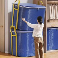 a woman standing in front of two large blue barrels next to a closet with clothes on it