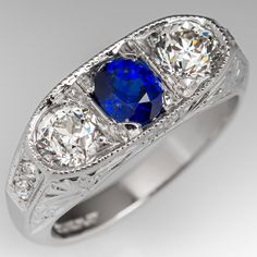 This lovely circa 1930s antique sapphire ring is centered with one (1), bead set, oval cut natural blue sapphire weighing 0.81 carats and flanked to each side by one (1), bead set, old European cut diamond. The shoulders of the ring are each bead set with two (2) round single cut diamonds. The gemstones are bordered with milgrain edging. Engraved details accent the side faces of the ring. The ring measures 7.3mm at the top, rises 3.7mm above the finger, tapering to 2.9mm wide and 1.6mm thick at Classic Sapphire Rings In Platinum, Oval Platinum Sapphire Ring, Classic Blue Sapphire Ring In Platinum, Vintage Sapphire Ring With Diamond Cut, Oval Shape, Vintage Oval Sapphire Ring With Diamond Cut, Classic Oval Sapphire Ring, Oval Sapphire Ring With Diamond Cut In Platinum, Art Deco Oval Sapphire Ring In Platinum, Vintage Oval Sapphire Ring In Platinum