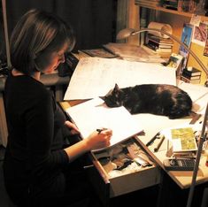 a woman sitting at a desk with a cat laying on top of her book and papers