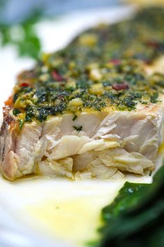 a white plate topped with fish covered in sauce and greens next to broccoli