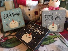 three snowman signs sitting on top of a table next to candles and other decorations