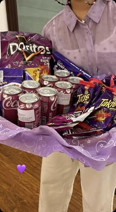 a woman holding a large basket filled with candy and snacks on top of a wooden table