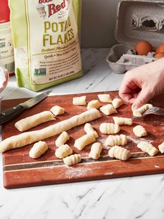 a person is cutting up some food on a wooden board next to eggs and flour