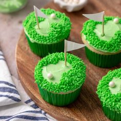 cupcakes with green frosting and white flags on top are sitting on a wooden plate