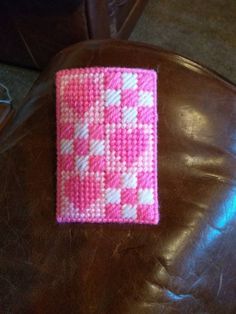 a pink and white knitted cell phone case sitting on top of a brown leather chair