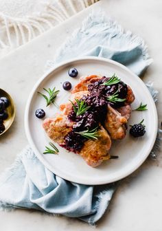 a white plate topped with meat covered in blueberry sauce and garnished with fresh herbs