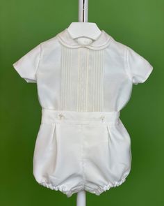 An elegant two-piece set for baby boys to wear during any special occasion. The top has a peter pan collar, geometrical frontal lace, handmade pleats, and short sleeves; it has buttons on the back for closure. The bottom is bubble shorts with buttons on the sides for closure and an elastic band on the back. The interior, or lining, is made with cotton fabric, while the exterior is with off-white organza. Dry clean 2 piece set Interior: 100% cotton; exterior: 100% polyester Made in Spain Final Sa Elegant Fitted Sets With Pintucks, Elegant Cream Short Sleeve Sets, Classic Fitted Short Sleeve Sets, Elegant White Short Sleeve Sets, Fitted Short Sleeve Sets For First Communion, Classic Short Sleeve Sets For Baptism, White Short Sleeve Formal Sets, Elegant Short Sleeve Baptism Sets, Baptism Outfits For Boys