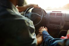 two people holding hands while sitting in a car with the driver's hand on the steering wheel