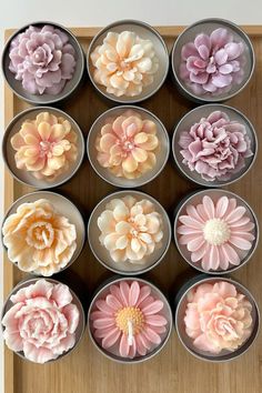 twelve pink and yellow flowers are in small metal bowls on a wooden tray with white background