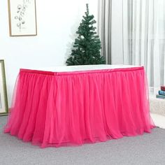 a pink tulle skirted table with a christmas tree in the corner behind it