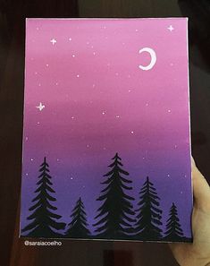 a hand holding up a card with trees and the moon in the sky on it