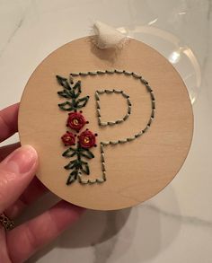 a hand holding a wooden ornament with flowers on it and the letter p