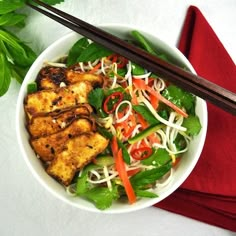 a white bowl filled with salad and chopsticks on top of a red napkin