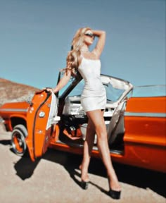 a woman standing next to an orange car with her hand on the door handle,