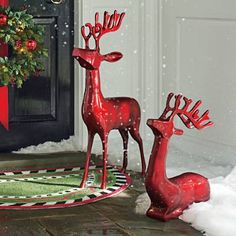 two red metal reindeer statues sitting on top of a rug next to a black door