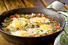 an iron skillet filled with eggs on top of a wooden table next to a green and white napkin