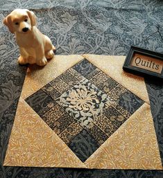 a dog sitting on the floor next to a quilted table top with a sign that says quilts