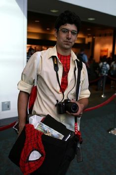 a man dressed as spider - man holding a camera in his right hand and wearing a red tie