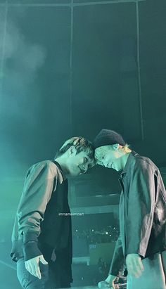 two young men standing next to each other in front of a stage with lights on