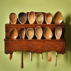 wooden spoons are lined up on a rack against a green wall with hooks and pegs