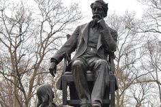 a statue of a man sitting on top of a chair next to a dog in front of trees