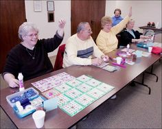 four elderly people sitting at a table playing board games with their hands in the air