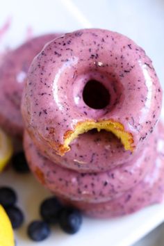 two doughnuts with purple icing and blueberries on a plate next to lemon slices