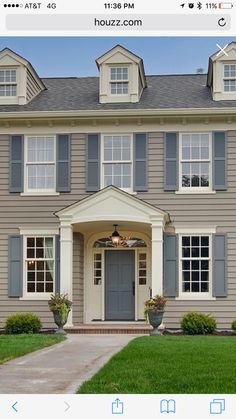 a large gray house with two story windows and blue shutters on the front door