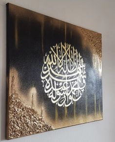 a painting with gold and black colors on the side of a white wall, depicting an islamic calligraphy