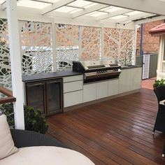 an outdoor kitchen with grill and table on wooden decking next to brick building area