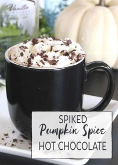 a black mug filled with whipped pumpkin spice hot chocolate on top of a white plate