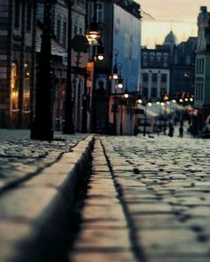 an empty cobblestone street at dusk with buildings in the background