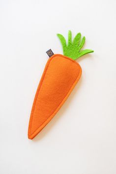 an orange felt carrot with green leaves on it's tip, sitting on a white surface