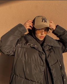 a person wearing sunglasses and a hat standing in front of a wall