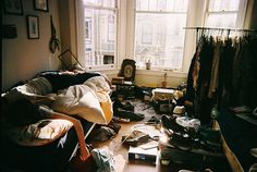 a messy room with lots of clutter on the floor and windows in the background