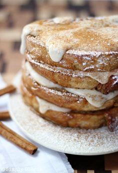 a stack of pancakes covered in powdered sugar on top of a white plate with cinnamon sticks