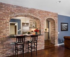 a living room filled with furniture next to a kitchen and dining room table in front of a brick wall