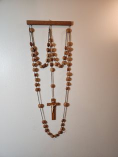 a wooden cross hanging from the side of a white wall next to a beaded necklace