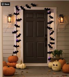 a front porch decorated for halloween with pumpkins and bats on the door, lights in the background